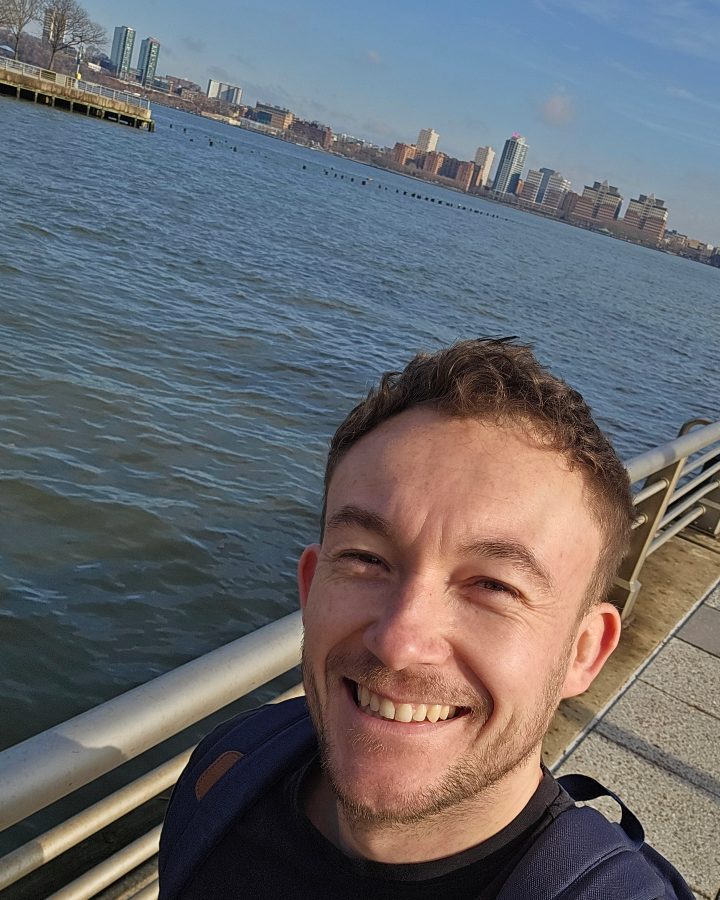 Matt Batey, photographed on a waterfront with a city skyline behind